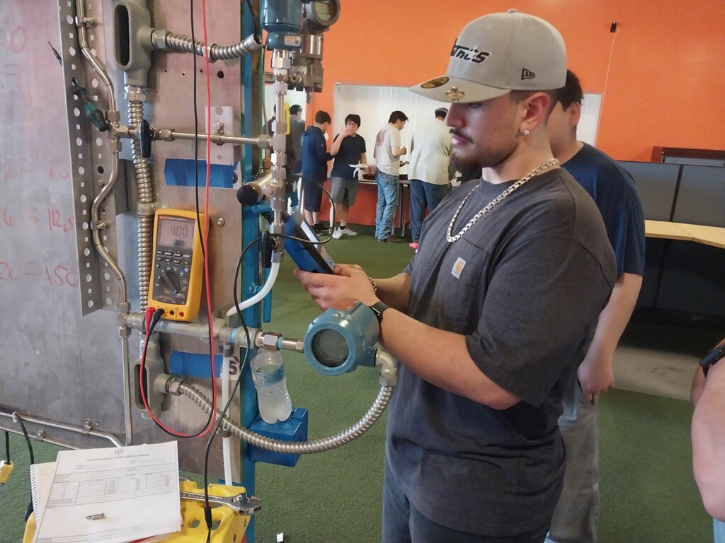 male student in blue shirt and safety glasses working on an industrial instrument in class