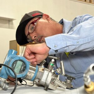 male student in blue shirt and safety glasses working on an industrial instrument in class